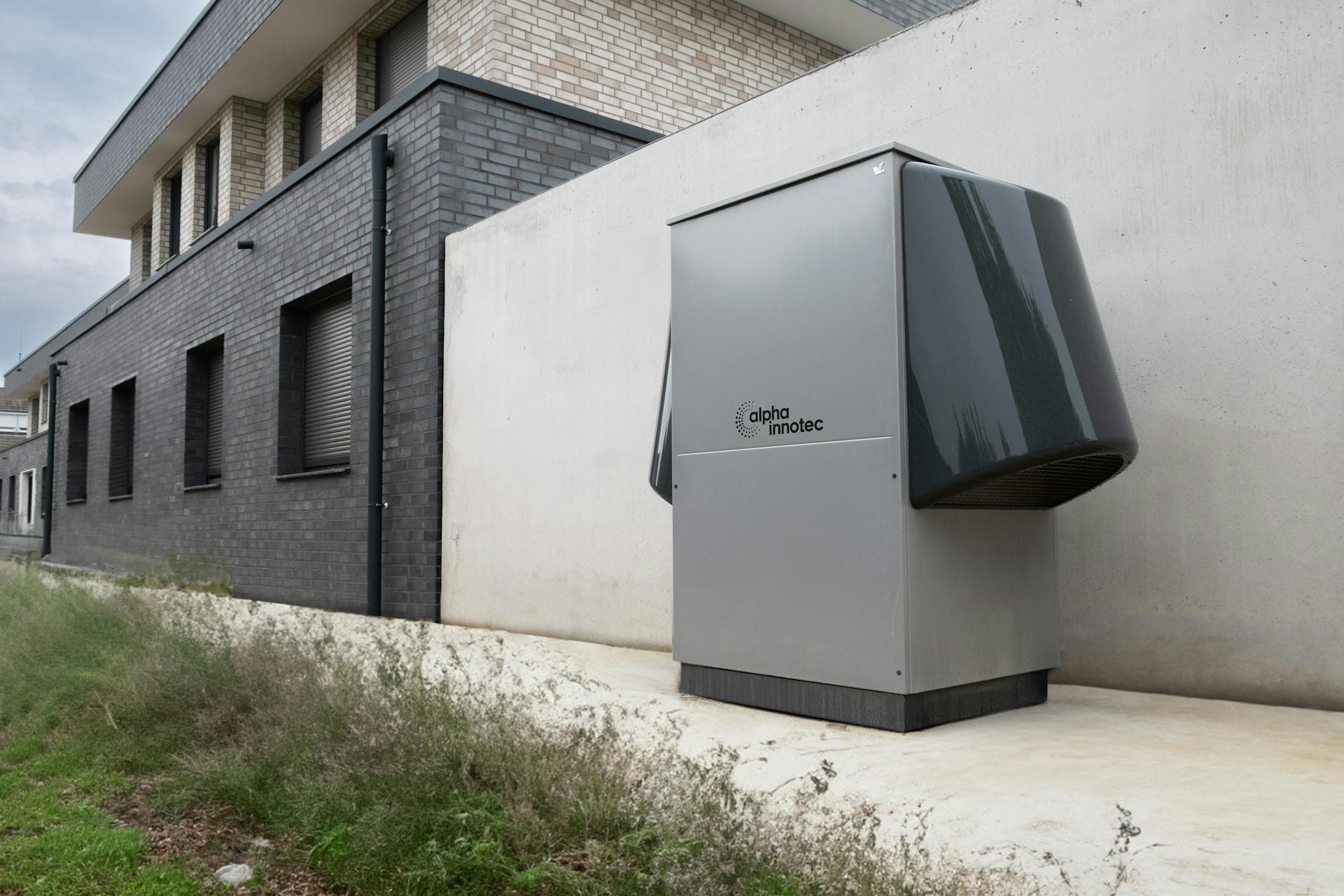 An air-source heat pump outdoor unit against the wall of a modern brick building
