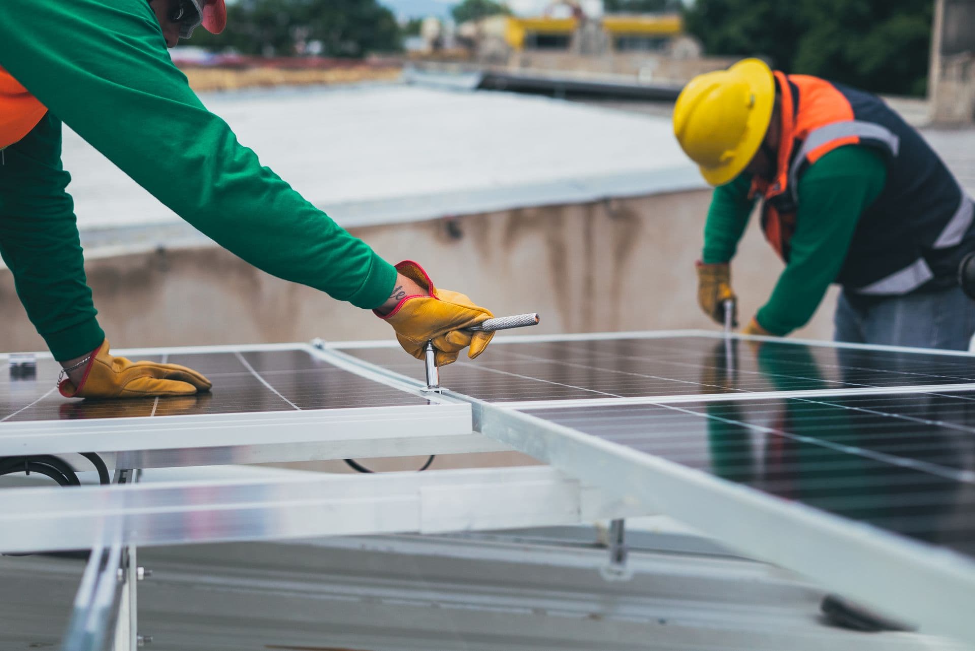Two installers fixing solar panels to mounting rails on a flat roof